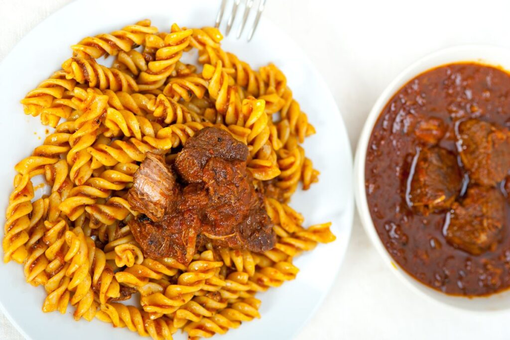 Pasta condita con un ricco ragù napoletano (carne e sugo di pomodoro) servita in un piatto bianco, vista dall'alto.