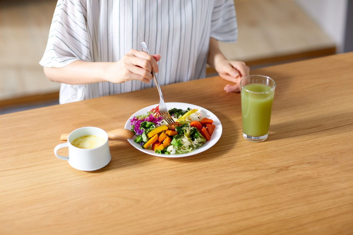 Primo piano di una persona che mangia un'insalata con un succo verde e una tazza di tè/bevanda calda su un tavolo di legno.