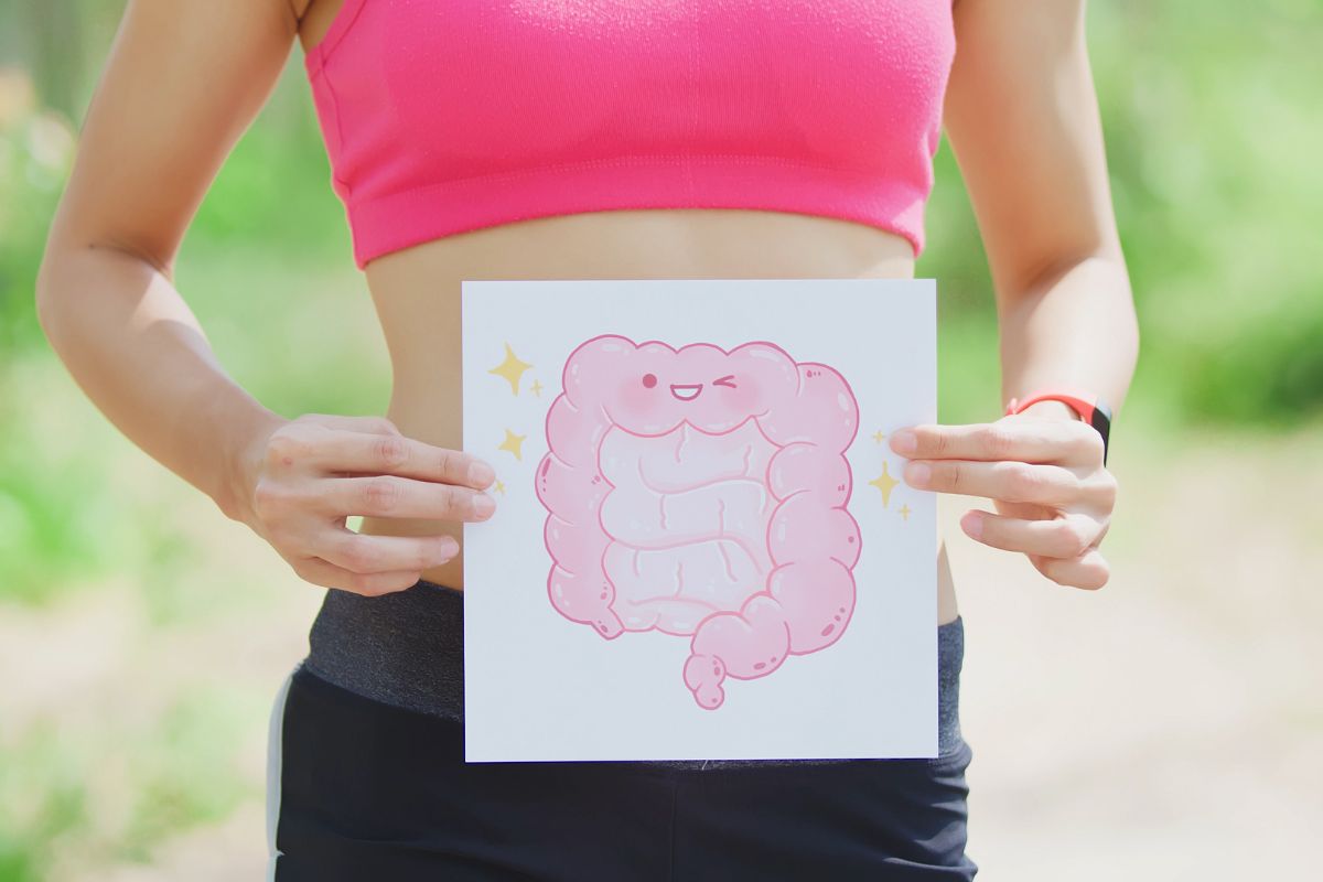 Donna sportiva che tiene in mano un disegno stilizzato e sorridente dell'intestino (intestino felice), rappresentando la salute digestiva.
