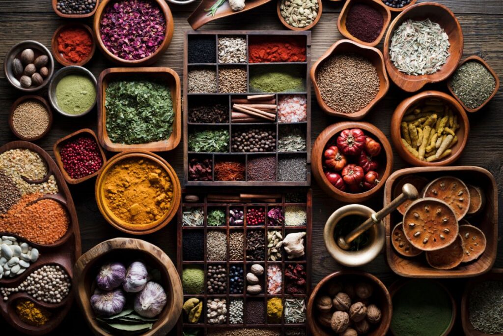 Assortimento colorato e abbondante di spezie e ingredienti naturali per la cucina, con mortaio, aglio e noci, su sfondo di legno scuro.