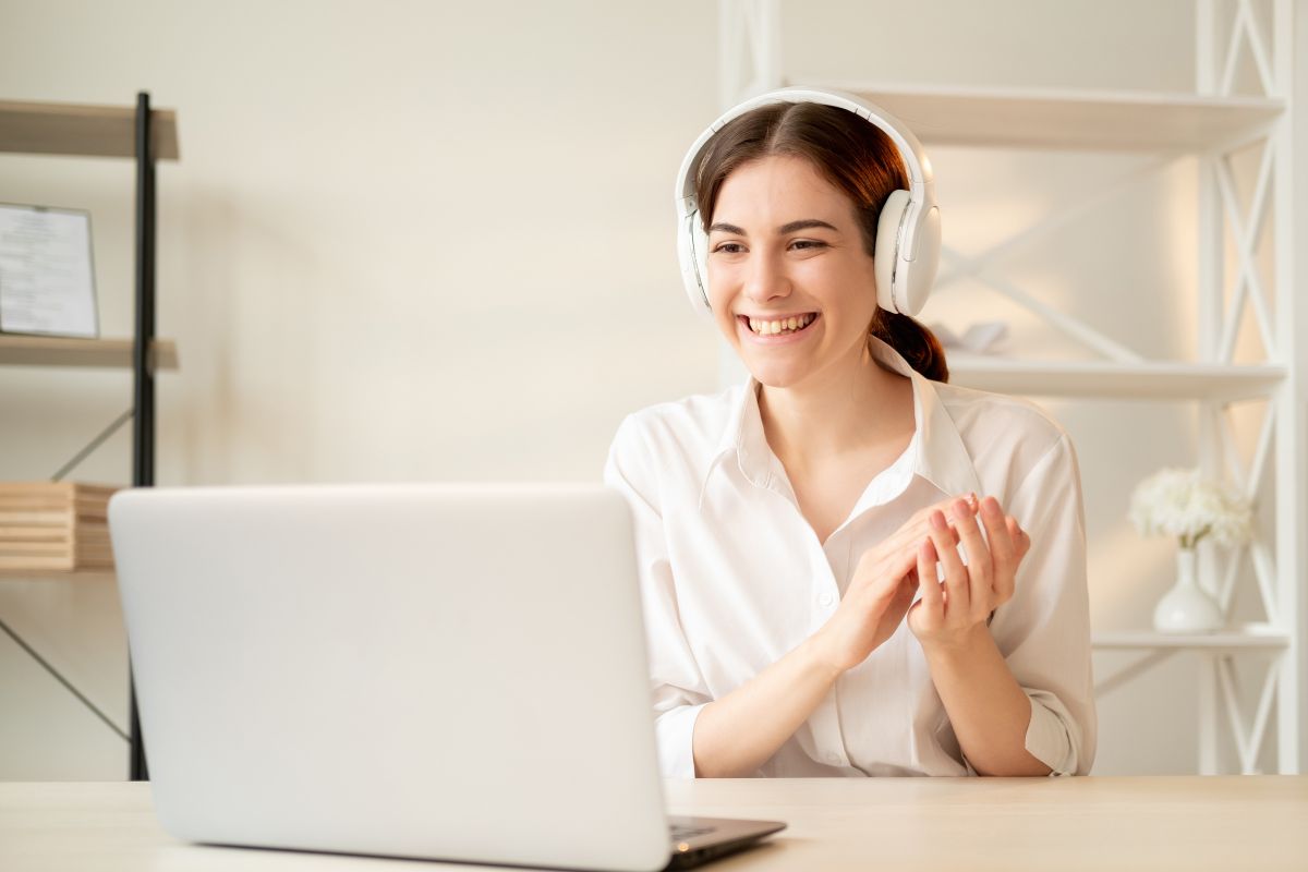 Giovane donna sorridente con cuffie bianche durante una videochiamata di coaching al laptop.