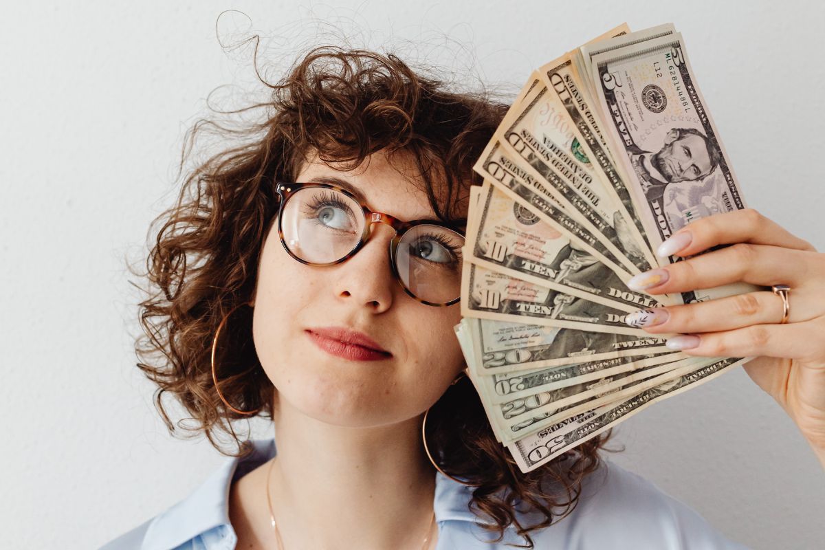 Una donna con gli occhiali che tiene in mano dei dollari.