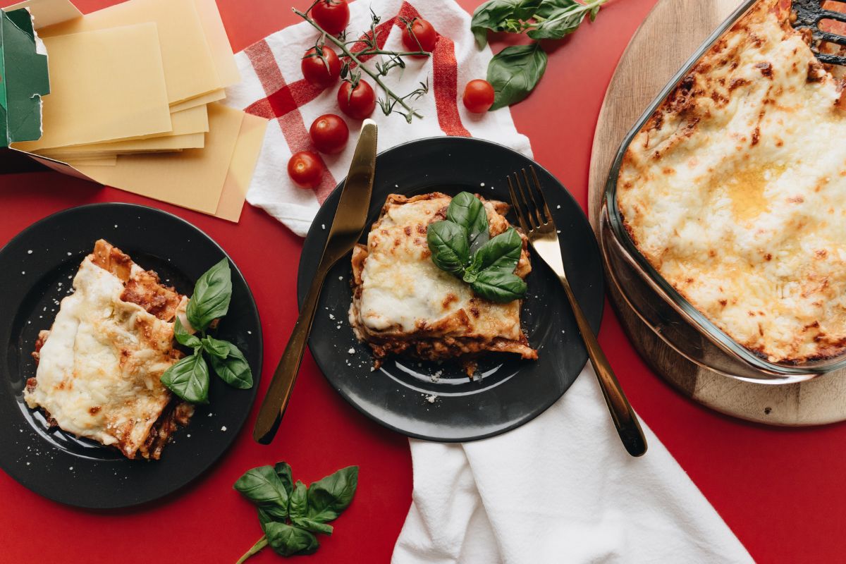 Porzione di lasagna al forno con crosticina dorata e basilico su un piatto nero elegante.