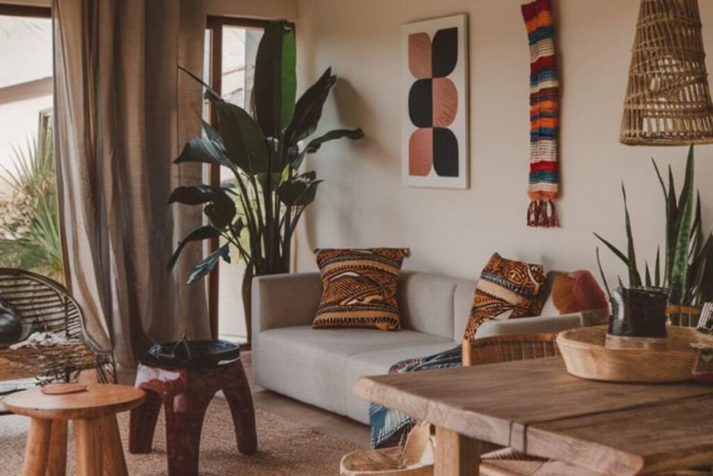 Soggiorno in stile boho o etnico con piante, divano neutro, cuscini a fantasia e mobili in legno.