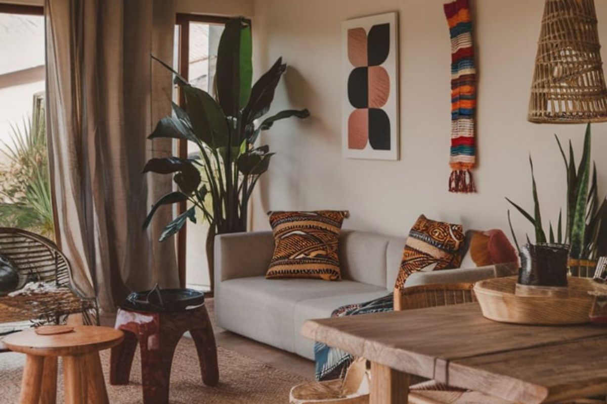 Soggiorno in stile boho o etnico con piante, divano neutro, cuscini a fantasia e mobili in legno.