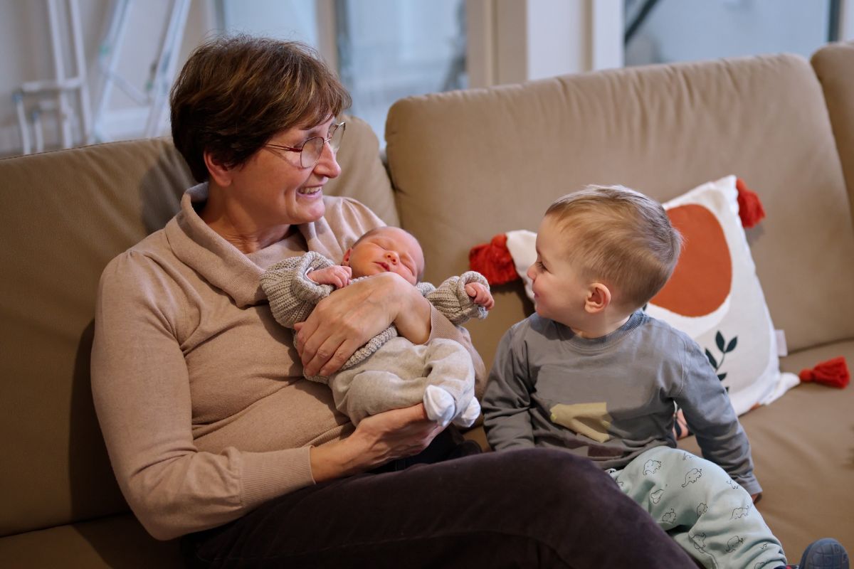 Nonna sorridente con due nipoti (un neonato e un bambino) sul divano.
