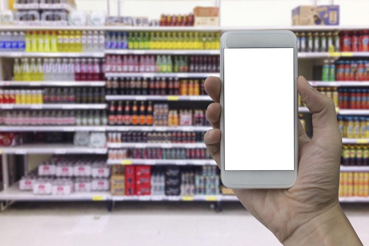 mano con telefono e scaffali supermercato