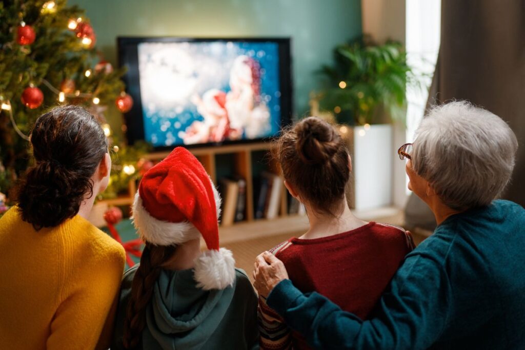 Famiglia seduta sul divano che guarda un film di Natale in TV accanto a un albero addobbato.