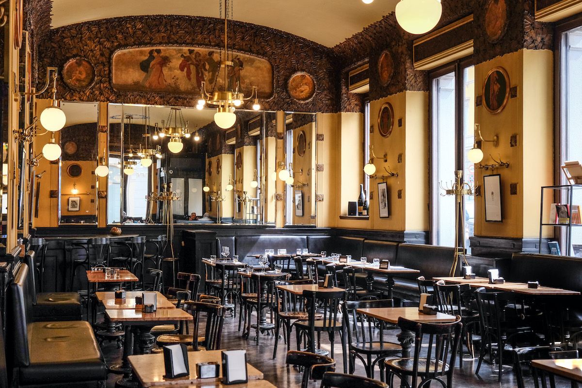 Interno di un caffè letterario storico italiano con specchi, decorazioni Liberty e tavoli neri apparecchiati.
