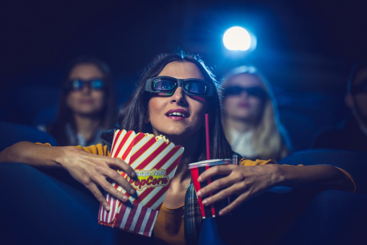 Donna al cinema con occhiali 3D, popcorn e bibita mentre guarda un film.