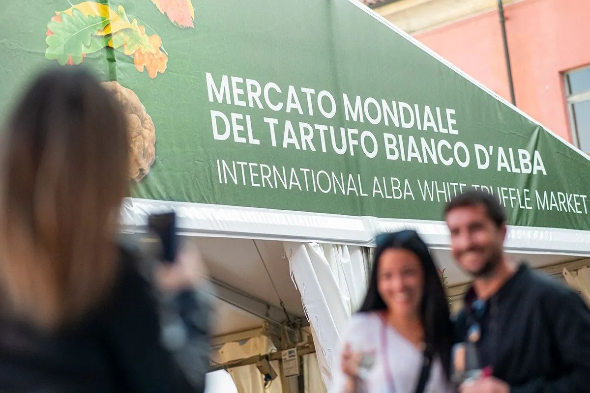 Coppia sorridente al Mercato Mondiale del Tartufo Bianco d'Alba sotto il tendone verde, fiera internazionale Langhe Piemonte.