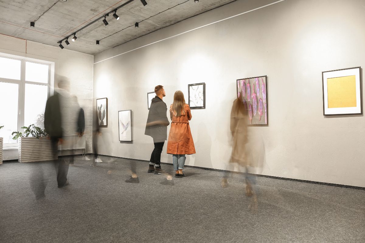 Interno di una galleria d'arte contemporanea con visitatori che osservano quadri alle pareti bianche.