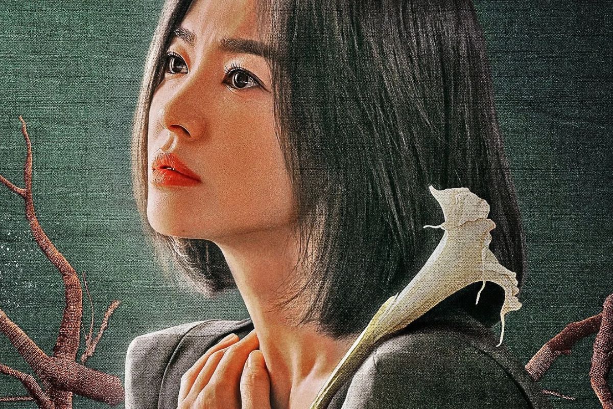 Primo piano dell'attrice Song Hye-kyo nei panni di Moon Dong-eun della serie Netflix The Glory, con uno sguardo determinato e un fiore di giglio bianco sulla spalla.